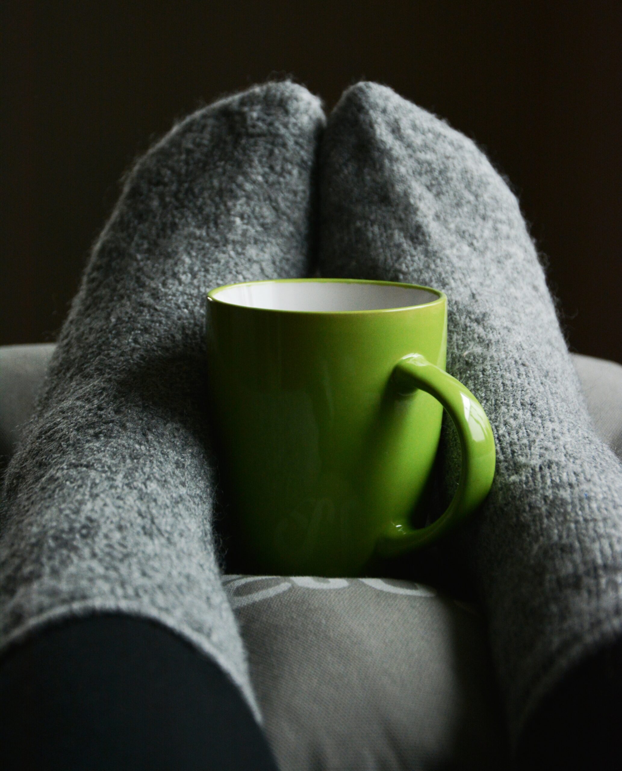 socked feet hugging a green mug