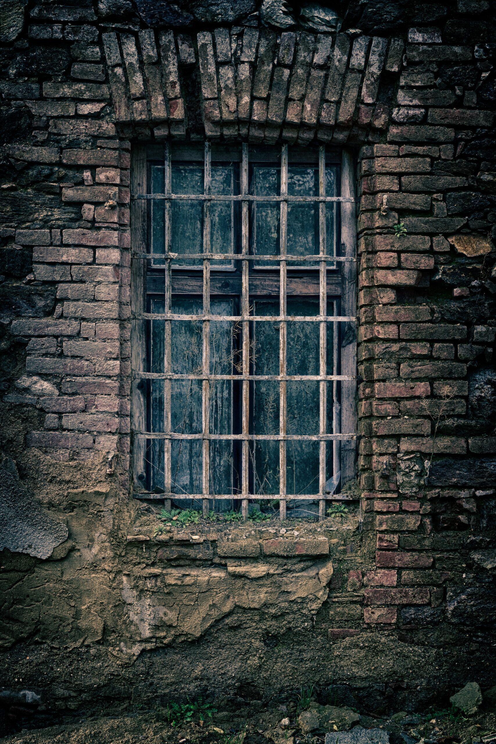 old, barred window in crumbling brick wall