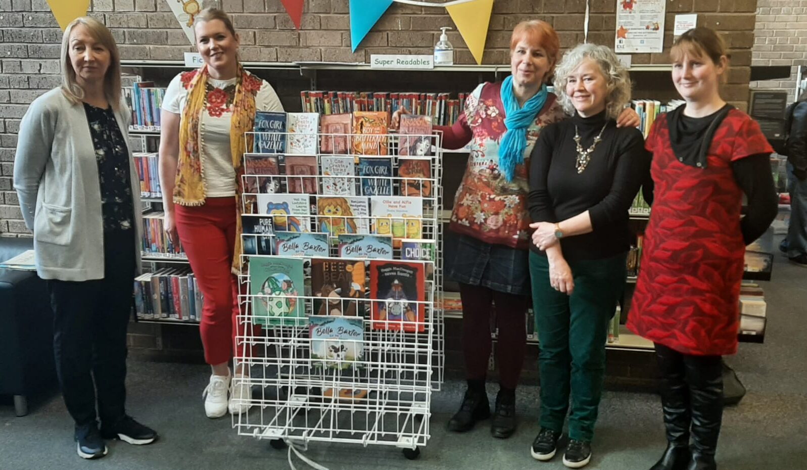 Paula standing in a group around a book display with other children's authors at Milngavie Library for World Book Day 2023